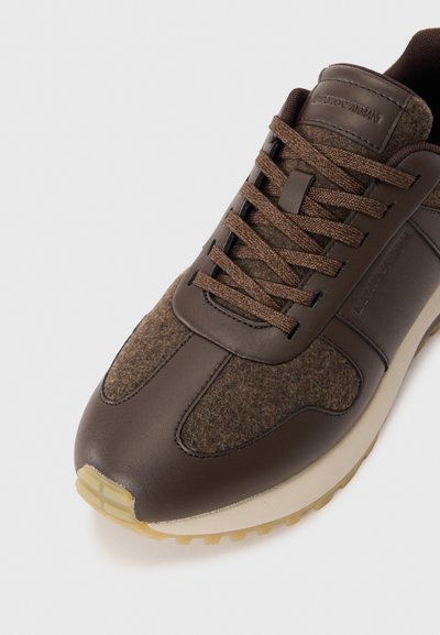 Brauner Sneaker mit Obermaterial aus Leder und Filz-Akzenten. Verfügt über braune Schnürsenkel, eine abgerundete Spitze und eine hellfarbige Gummisohle.