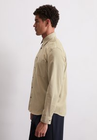 Licht khaki langemouwen shirt met een knoopsluiting aan de voorkant, een borstzak en een relaxte pasvorm, vervaardigd van een zachte, gladde stof.