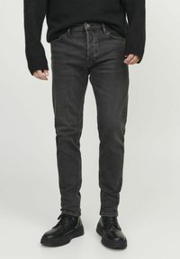Čierne denimové džínsy so slim fit strihom, obsahujúce predné vrecká, zips a diskrétne šitia. V páre s čiernymi šnurovacími čižmami.