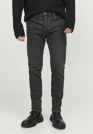 Melnas denim bikses ar šauru piegriezumu, aprīkotas ar priekšējām kabatām, rāvējloku un smalkiem dūriem. Saskaņotas ar melniem šņorējamiem zābakiem.
