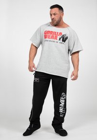 Gray oversized t-shirt with red "GORILLA WEAR" print and black pants displaying "Gorilla Wear" in silver. Both offer a relaxed fit.