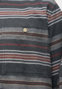 Ciemnoszara tkanina z poziomymi paskami w kolorze białym, czerwonym i beżowym, z przednią kieszenią ozdobioną beżowym guzikiem.