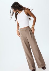 Biely bezrukávový crop top v kombinácii s voľnými nohavicami s béžovými prúžkami. Hladká textúra, vysoký pás a široký strih nohavíc.
