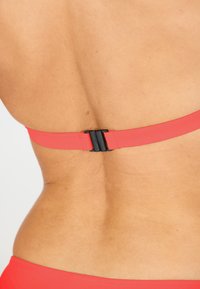 Rode bikini-top met een gladde, matte afwerking. Voorzien van een zwarte plastic sluiting aan de achterkant. Eenvoudige, verstelbare bandjes maken het ontwerp compleet.