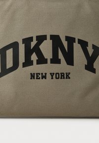 Sac fourre-tout DKNY en matériau kaki texturé, présentant un grand logo noir avec l'inscription "DKNY NEW YORK" bien centrée.