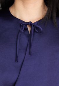 Mornariće plavi top s okruglim izrezom i malim detaljem mašne na ovratniku. Glatka tkanina s mekim teksturom i urednim šavovima.