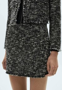 Zwart-witte tweed blazer met franjes, textuurstof en een twee-delige ontwerp, met een open voorkant en minimale details.