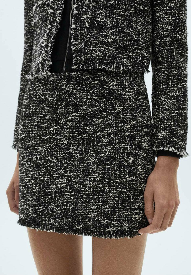 Zwart-witte tweed blazer met franjes, textuurstof en een twee-delige ontwerp, met een open voorkant en minimale details.