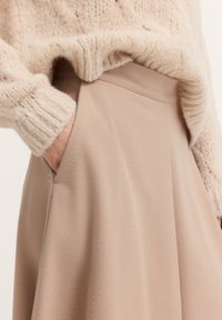 Beige Rock mit glatter Textur, hoher Taille und seitlichen Taschen, kombiniert mit einem leichten, gestrickten beigen Pullover.