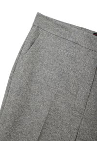 Gros plan d’un pantalon en laine gris montrant la ceinture et la poche latérale avec un tissu finement texturé.