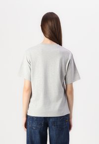 Grå kortermet t-skjorte i en avslappet fasong med rund hals, kombinert med mørkeblå denim-bukser med baklommer.
