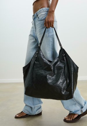 Black leather tote bag with a slouchy design, featuring two straps and silver hardware accents. Textured surface and spacious interior.