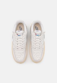 Białe skórzane trampki z perforowanym noskiem, płaskimi sznurowadłami i beżową gumową podeszwą. Na języku i bokach znajduje się wielokolorowe logo Nike.