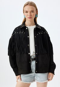 Zwarte suede jas met franjes op de mouwen en metalen studs op de schouders. Knopsluiting en een relaxed fit ontwerp.