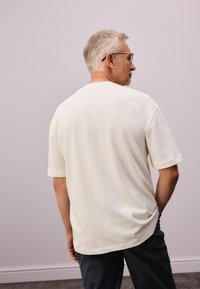 Kortærmet cremeshirt med en afslappet pasform. Lavet af blødt stof, med rund hals og en glat tekstur, parret med mørke bukser.