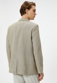 Beige blazer tillverkad av strukturerad tyg, med en klassisk design, snedskurna slag, enkel vent bak, och knappar på ärmarna.