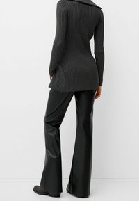 Long, ribbed, dark gray sweater with a draped collar paired with high-waisted, black faux leather flared pants. Smooth texture, fitted design.