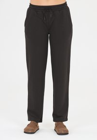 Dunkelgraue Sweatpants mit einem elastischen Bund, Zugbanddetails, seitlichen Taschen und einer lockeren Passform. Kombiniert mit braunen Slippern.