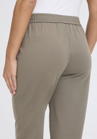 Olivgrüne, leichte Stoffhosen mit elastischem Bund, die eine glatte Textur und ein schmal zulaufendes Bein-Design aufweisen.