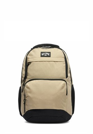 Beige og sort Billabong rygsæk med flere lynlåslommer og netlommer på siderne mod hvid baggrund.