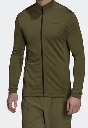 Mand iført olivengrøn langærmet lynlåstrøje og matchende bukser, med diskret "TERREX"-logo på bryst og lår.