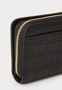 Black wallet with textured crocodile pattern and gold zipper along the edge, shown from a close-up angled side view.