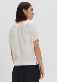 Crème kortemouwen top met een textuur van ribbenpatroon. Relaxte pasvorm met zijsplitten en een ronde halslijn. Glad, lichtgewicht stof.