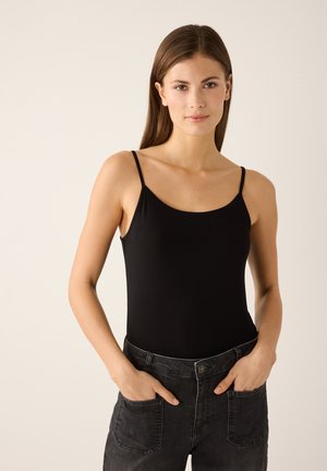 Schwarzer ärmelloser Body mit dünnen Trägern aus weichem Material. Kombiniert mit hoch taillierten dunkelgrauen Jeans mit Fronttaschen.