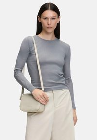 Szary prążkowany longsleeve, beżowa torba na ramię. Torba ma gładką teksturę i subtelne logo, noszona z jasnymi spodniami.