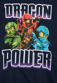 Navy T-shirt featuring three colorful cartoon ninjas in green, red, and blue, with bold text reading "DRAGON POWER" in white and purple gradient.