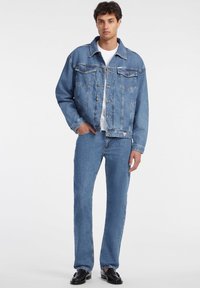 Light blue denim jacket with two chest pockets and front buttons, paired with matching denim jeans. Both garments have a smooth texture.