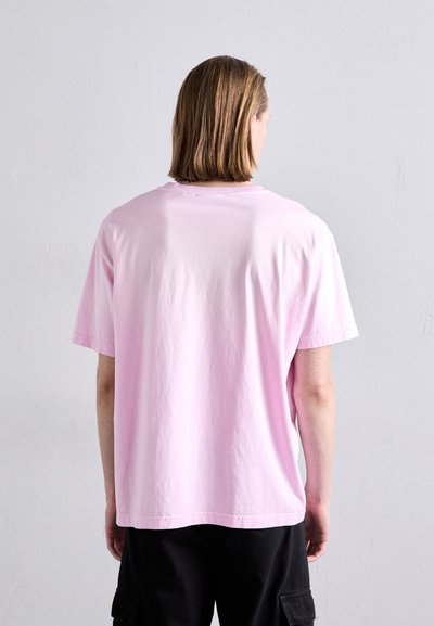 T-shirt en coton rose clair avec une coupe décontractée, un col rond et des manches courtes. Design minimaliste, sans logos ni motifs visibles.