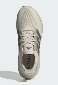 Zapatilla de running de punto beige con rayas gris claro, cordones blancos y texto "ULTRABOOST" visible en la plantilla, vista desde arriba.