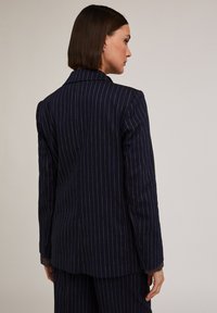 Blazer a righe blu navy con design strutturato, rever a notchy, tessuto testurizzato e cuciture visibili ai polsini.