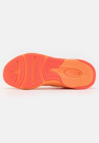 Sulan på en träningsskor i ljus orange och persiko färger, med texturerade hexagonala mönster och spår för grepp.