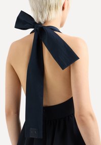 Abito senza schienale di colore blu navy con un grande fiocco al collo, tessuto liscio e vita aderente con un'etichetta di marca vicino alla cerniera.