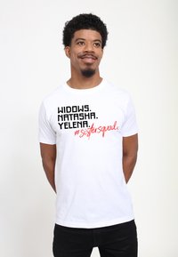 Hvid bomulds T-shirt med fed sort og rød tekst: "WIDOWS. NATASHA. YELENA. #sistersquad." Klassisk rund hals, korte ærmer.