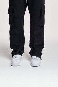 Pantalons cargo noirs avec plusieurs poches latérales, coupe décontractée et chevilles resserrées ; associés à des baskets blanches. Tissu en coton texturé.