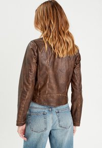 Bruine leren jas met een getailleerd ontwerp, voorzien van een cropped lengte, schoudernaad en subtiele stikdetails. Gecombineerd met blauwe spijkerbroeken.