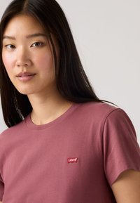 Μακρυμάνικη βαμβακερή μπλούζα σε μπορντό χρώμα, με κοντά μανίκια και κόκκινο λογότυπο Levi's στο αριστερό μέρος του στήθους. Απλός, κλασικός σχεδιασμός.