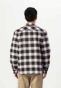 camisa de franela a cuadros en colores negro, blanco y rojo; cuenta con un cuello abotonado y mangas largas con botones en los puños; dobladillo recto.