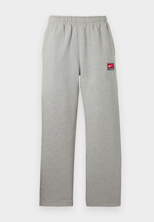 Pantalon de jogging gris avec une ceinture élastique, coupe droite, et un petit patch logo Nike rouge et blanc sur le côté gauche. Texture douce.