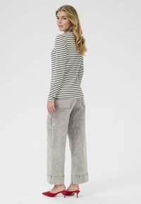 Maglia a maniche lunghe a righe in bianco e nero, abbinata a jeans a gamba larga grigio chiaro. Mule rosse con tacco alto, texture liscia e design casual.