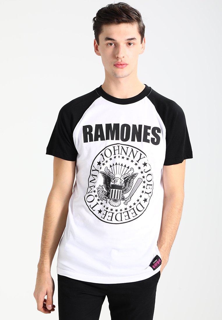 Camiseta de algodón en blanco y negro que presenta un gráfico circular con el texto "RAMONES" y un diseño de águila, mangas cortas y una etiqueta rosa.