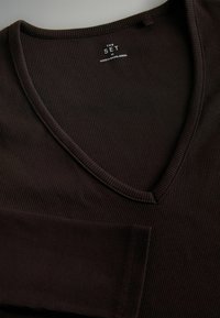Dunkelbraunes, geripptes Strickoberteil mit langen Ärmeln und V-Ausschnitt, ausgestattet mit einem Etikett mit der Aufschrift "THE SET", glatter Textur und tailliertem Design.