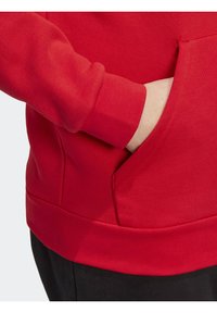 Röd sweatshirt med en mjuk textur, åtsittande mudd och en sidoficka med en dold dragkedja. Nederkanten är elastisk.