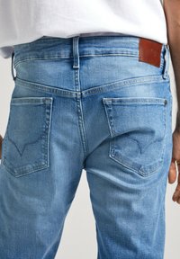 Jeans de mezclilla azul claro con un corte relajado, que cuentan con dos bolsillos traseros, costuras visibles y una etiqueta de cuero marrón en la cintura.