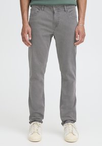 Szürke farmernadrág vékony szabással, ötpántos kialakítással és finom textúrával; ellensúlyozva törtfehér tornacipővel.