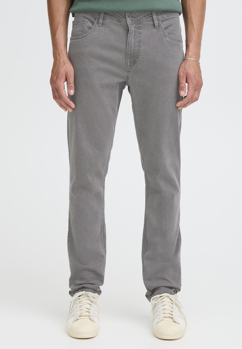 Szürke farmernadrág vékony szabással, ötpántos kialakítással és finom textúrával; ellensúlyozva törtfehér tornacipővel.