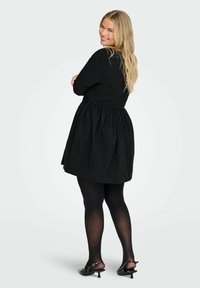 Melna kleita ar pieguļošu augšdaļu un izplesto svārku. Garas piedurknes, strukturēts audums, nēsāta ar melniem zeķturiem un papēžu kurpēm.